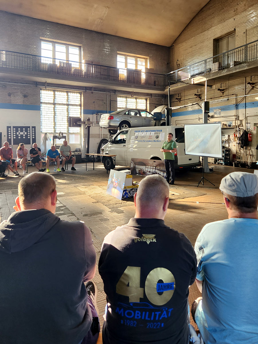 Eine Gruppe aus Auszubildenden und Mitarbeitern folgen einer Präsentation in der KFZ-Werkstatt